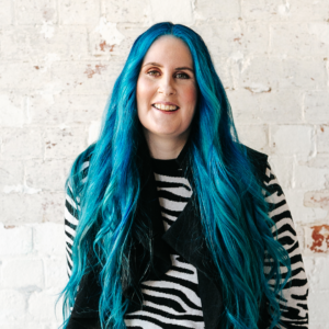 Photo of Bridget with blue hair, she's wearing a zebra top and is smiling.